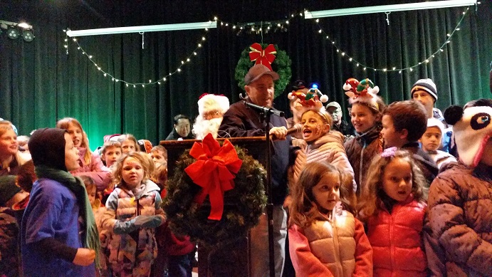 Mayor Leonard Desiderio holds the microphone for a child during a sing-along of holiday tunes with Santa on the stage at Excursion Park.