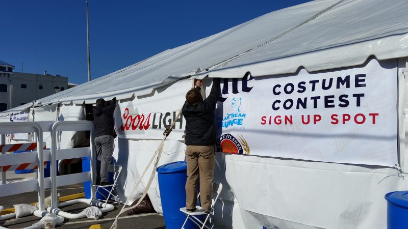 Workers attach a sign on an outdoor tent at the LaCosta Lounge, the social and entertainment epicenter for the weekend festivities.
